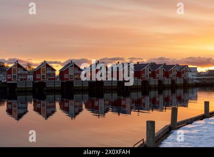 Svolvaer, Lofoten Inseln, Norwegen. Rote Holzhäuser im Hafen von Svolvær. Der Sonnenuntergang verleiht dem Himmel eine wunderschöne orange, gelbe und rosa Farbe. Stockfoto