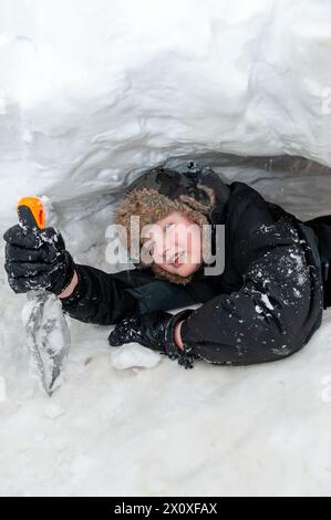 Kind, warm eingewickelt, spielt in einem Schneetunnel, der nach einem Schneesturm in eine Schneewolke gegraben wurde, Cumbria, Großbritannien. Stockfoto