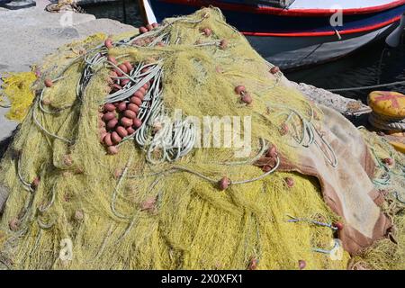 Gelbes Fischernetz mit Bojen auf dem Pier vor dem Fischerboot. Es ist viel Kopierraum vorhanden. Stockfoto