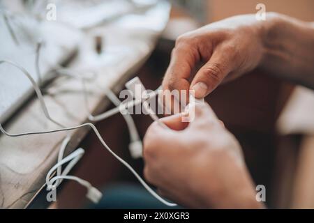 Verschränkte Lösungen – Eine Nahaufnahme der Hände, die sorgfältig das richtige Kabel aus einem verworrenen Sortiment auswählen, was die Komplexität und Präzision symbolisiert Stockfoto