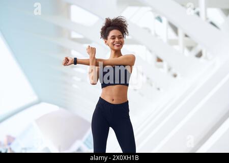 Eine Frau in Sportbekleidung lächelt, während sie im Fitnessstudio im Freien ihre Arme ausdehnt Stockfoto