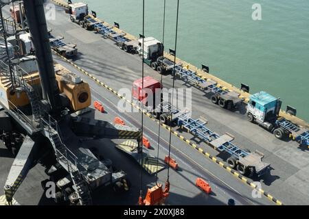 Alte LKWs im Containerterminal warten auf Verladung neben mobilen Kränen mit orangefarbenem Streuer, der von Staudörfern im Hafen von Puerto Barrios betrieben wird. Stockfoto