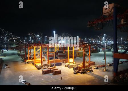 Moderner Containerterminal während des Nachthafens von La Guairá, beobachtet von einem Frachtschiff, das unter Portalkranen verankert ist. Stockfoto