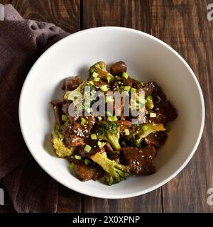 Rindfleisch mit Brokkoli in der Schüssel über hölzernem Hintergrund. In dünne Scheiben geschnittenes Rindfleisch mit geröstetem Brokkoli. Nahansicht Stockfoto