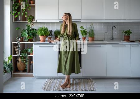 Zufriedene Geschäftsfrau in Gläsern mit Glas Wasser, die in der Küche zu Hause steht Stockfoto