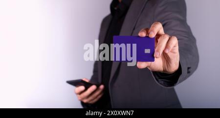 Geschäftsmann hat eine leere lila Kreditkarte. Mann im Anzug, weißer Hintergrund, das Handy hält Stockfoto