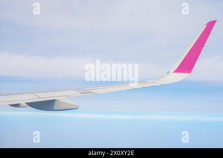 Blick vom Fenster auf den Flügel eines Flugzeugs, das über Meer und Wolken fliegt. Stockfoto