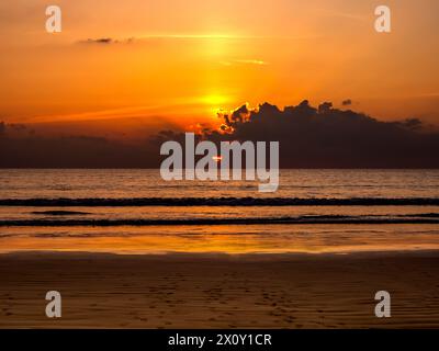 Wunderschöner Hintergrund des Sonnenunterganghimmels mit Sonnenstrahlen hinter schwarzer Wolke über dem Meerwasser. Dunkle Landschaft und Ozeanszene. Sommer Sandstrand am Abend t Stockfoto