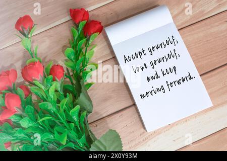 Motivationszitat auf Notizbuch geschrieben mit künstlichen Blumen auf Holztisch Stockfoto