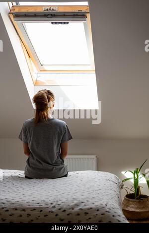 Rückansicht einer allein depressiven weiblichen Person sitzt auf dem Bett im Schlafzimmer vor dem Fenster. Stockfoto
