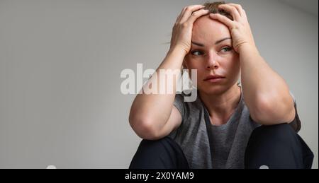 Porträt einer heruntergekommenen und depressiven erwachsenen Frau zu Hause. Niedergedrückte Frau, die den Kopf in den Händen hält. Stockfoto