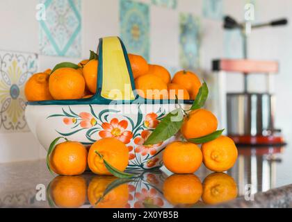 Clemantinen in einer Keramikschale auf einer reflektierenden Arbeitsplatte aus Granit mit Entsafter Stockfoto