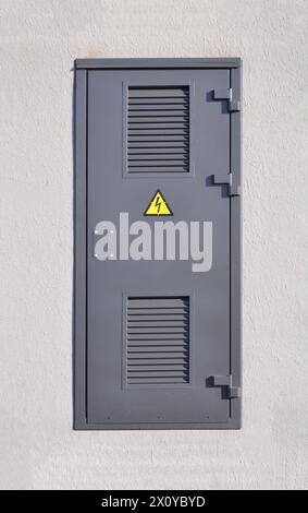 Graue Metalltür gegen eine weiße Wand. Elektrische Gefahr. Transformator. Stockfoto