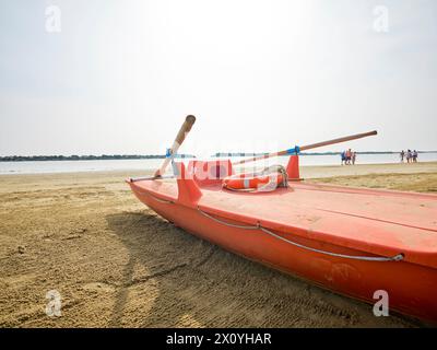Rettungsboot im Vordergrund am Strand an einem sonnigen Sommermorgen, im Hintergrund einige Badende kühlen sich an der Adriaküste, Italien. Stockfoto