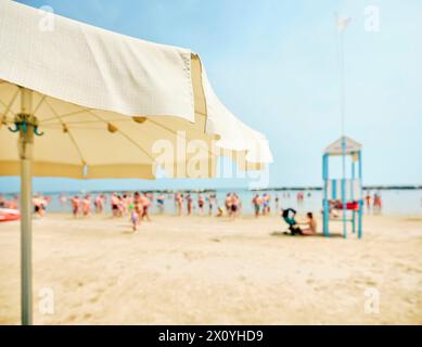 Blick auf den Strand von einem Sonnenschirm mit einem Rettungsschirm neben einem Rettungsboot am Strand an einem sonnigen Sommertag, im Hintergrund einige Schwimmer Ref Stockfoto