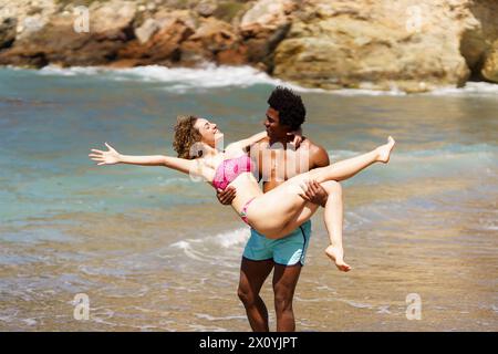 Abwechslungsreiches Paar, das bei Tageslicht am Strand Spaß hat Stockfoto