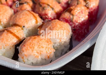Gebackene Sushi-Brötchen mit Lachs, Käse und Sauce auf einem geschäumten Polystyrol-Tablett aus nächster Nähe. Stockfoto