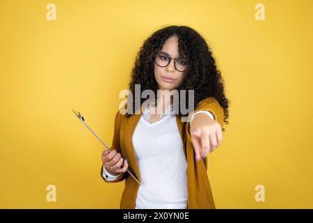 afroamerikanische Geschäftsfrau mit Papierkram in den Händen über gelbem Hintergrund, die mit dem Finger auf die Kamera zeigt und auf dich, selbstbewusste Gestensuche Stockfoto