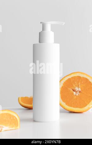 Weiße Kosmetik-Shampoo-Spender-Flasche Mockup mit Orangen auf einem weißen Tisch. Stockfoto