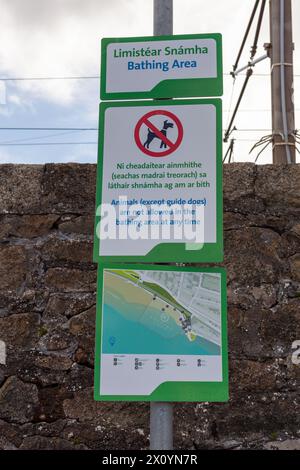 Straßenschild mit einem Badegebiet mit einer Karte und einem Schild, das Haustiere aus dem Gebiet vor einer Steinmauer verbietet. Es gibt elektrische Leitungen hinten Stockfoto