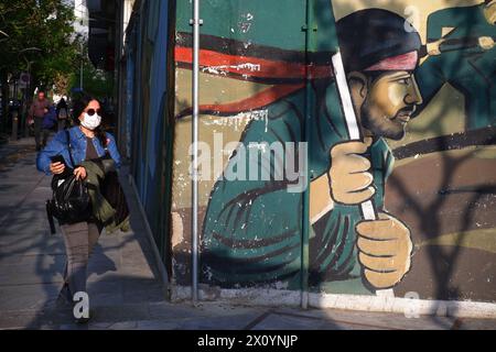 Teheran, Iran. April 2024. Eine iranische junge Frau, die eine Gesichtsmaske trägt, ohne ihr obligatorisches islamisches Kopftuch zu bedecken, geht neben einem Wandgemälde von Soldaten der iranischen Revolutionsgarde (IRGC) auf dem Palästinensischen Platz in der Innenstadt von Teheran. Israel feierte am Sonntag seine Luftverteidigung angesichts eines beispiellosen Angriffs des Iran und sagte, dass die Systeme 99 % der mehr als 300 Drohnen und Raketen, die auf sein Territorium abgefeuert wurden, vereitelten. (Kreditbild: © Rouzbeh Fouladi/ZUMA Press Wire) NUR REDAKTIONELLE VERWENDUNG! Nicht für kommerzielle ZWECKE! Stockfoto
