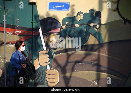Teheran, Iran. April 2024. Eine iranische junge Frau, die eine Gesichtsmaske trägt, ohne ihr obligatorisches islamisches Kopftuch zu bedecken, geht neben einem Wandgemälde von Soldaten der iranischen Revolutionsgarde (IRGC) auf dem Palästinensischen Platz in der Innenstadt von Teheran. Israel feierte am Sonntag seine Luftverteidigung angesichts eines beispiellosen Angriffs des Iran und sagte, dass die Systeme 99 % der mehr als 300 Drohnen und Raketen, die auf sein Territorium abgefeuert wurden, vereitelten. (Kreditbild: © Rouzbeh Fouladi/ZUMA Press Wire) NUR REDAKTIONELLE VERWENDUNG! Nicht für kommerzielle ZWECKE! Stockfoto