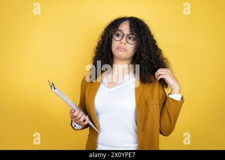 afroamerikanische Geschäftsfrau mit Papierkram in den Händen auf gelbem Hintergrund, die sein T-Shirt mit einem erfolgreichen Ausdruck lässiger Kleidung hält Stockfoto