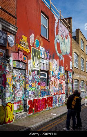 Brick Lane Street Art London, Passanten sehen Street Art in einer kleinen Straße in der Brick Lane, Shoreditch, East London. Stockfoto