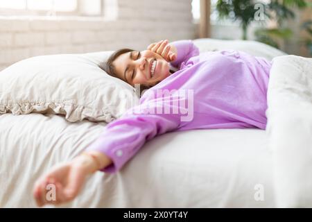 Entspannte Frau, die in einem lila Hemd auf dem Bett liegt Stockfoto