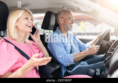 Eine ältere Frau telefoniert im Auto, ein Mann fährt glücklich Stockfoto