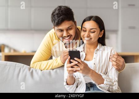 Ein junges Paar, das zu Hause zusammen auf das Smartphone schaut Stockfoto