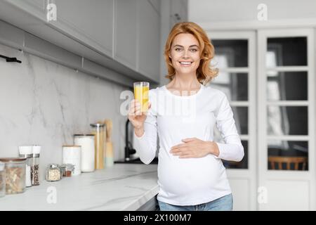 Lächelnde schwangere Frau mit Orangensaft in der Küche Stockfoto