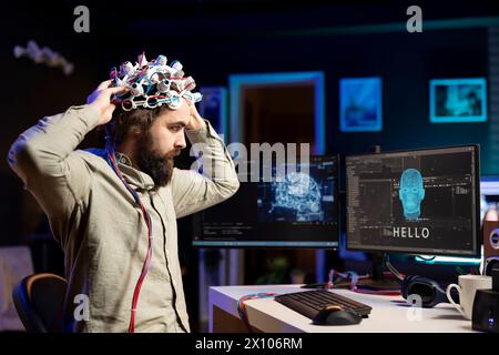 IT-Spezialist, der ein EEG-Headset aufsetzt, um mit künstlicher Intelligenz auf dem Computer in Binärcode zu kommunizieren. Software-Ingenieur sendet Gehirnwellensignale an empfindungsfähige KI auf PC mit High-Tech-Gerät Stockfoto
