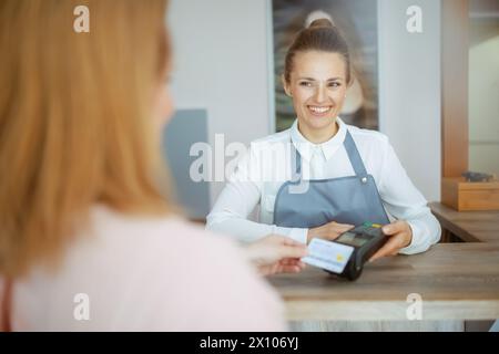 Friseurin in modernem Schönheitsstudio, Gäste akzeptieren Kreditkartenzahlungen über das Terminal an der Rezeption. Stockfoto