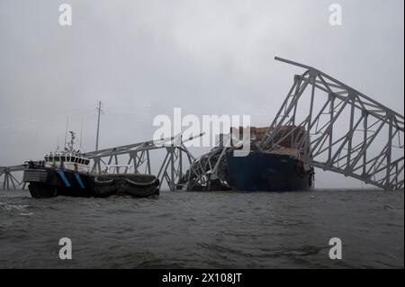 Dundalk, Vereinigte Staaten von Amerika. April 2024. Ein Bergungsschiff greift auf den Schaden des verwickelten Frachtträgers MV Dali zu, der in den Stahlträgern der eingestürzten Francis Scott Key Bridge, die den Kanal Fort McHenry blockiert, am 3. April 2024 in der Nähe von Dundalk, Maryland, eingehüllt ist. Die Brücke wurde am 26. März von einem 984-Fuß-Containerschiff getroffen und stürzte zusammen, wobei sechs Arbeiter ums Leben kamen. Quelle: PO2 Alejandro Rivera/US Coast Guard/Alamy Live News Stockfoto