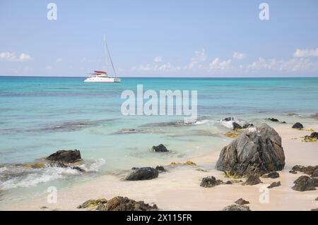 Ein kleines Boot segelt im Meer in der Nähe eines felsigen Ufers. Das Wasser ist ruhig und der Himmel ist klar Stockfoto