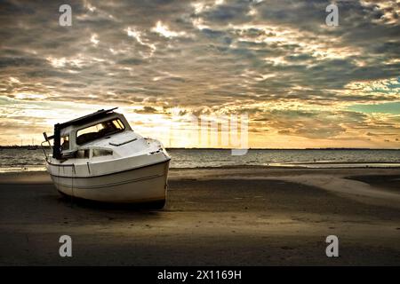 Boot ist am Strand gestrandet nach Sturm Sonnenuntergang dramatischer Himmel Stockfoto