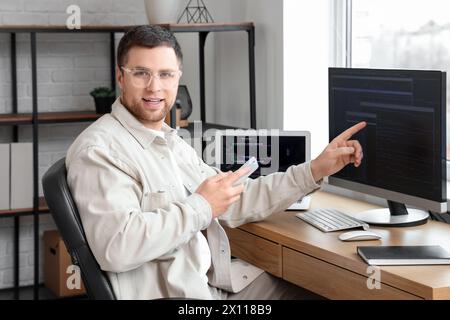 Porträt eines männlichen Programmierers, der im Büro auf den Computerbildschirm zeigt Stockfoto