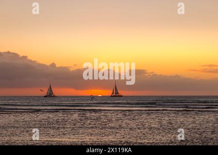 Segelboot und Windsurfer am Horizont mit untergehender Sonne Stockfoto