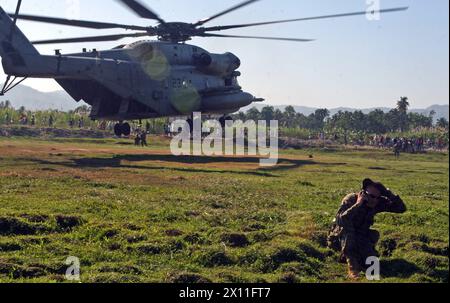 Gunnery Sergeant Joshua Wruble, Kompanie Gunnery Sergeant, Kilo Company, Bataillon Landing Team, 3. Bataillon, 2nd Marine Regiment, 22nd Marine Expeditionary Unit, unterhält Funkkontakt mit dem CH-53E Super Hengst der Marine Heavy Helicopter Squadron 461 (verstärkt), während es abhebt, nachdem es Nahrung und Wasser während einer Versorgungsmission in der Nähe von Leogane, Haiti, 22. Januar 2010 geliefert hat. Stockfoto