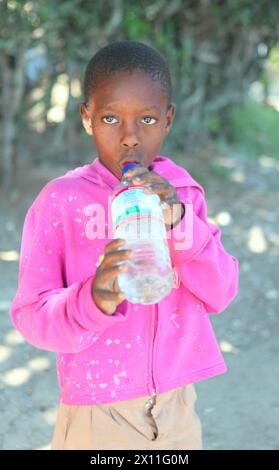 Ein haitianischer Junge hält an, um einen Drink Wasser zu nehmen, während Marines und Korps aus dem Battalion Landing Team, 3. Bataillon, 2. Marine Regiment, 22. Marine Expeditionary Unit, eine medizinische Standortuntersuchung in einem kleinen Dorf in der Nähe von Leogane, Haiti, am 22. Januar 2010 durchführen. Stockfoto
