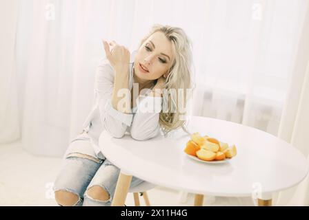 Eine Frau sitzt an einem Tisch mit einem Teller Persimmonen vor sich. Stockfoto