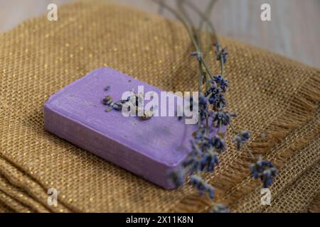 Lavendelseife auf Stoffhintergrund mit Kopierraum für Ihren Text. Anzeigenvorlage - Modell. Hautpflege hausgemachtes Naturkosmetikkonzept. Bio-trockene Lavendelblüte. Handgemachte Seife Stockfoto