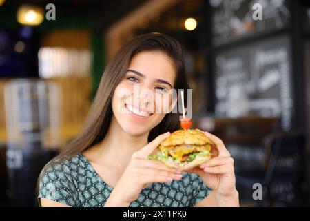 Eine glückliche Frau, die dich ansieht und Burger in einer Bar zeigt Stockfoto