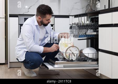 Mann, der in Innenräumen Geschirrspüler mit schmutzigen Tellern lädt Stockfoto