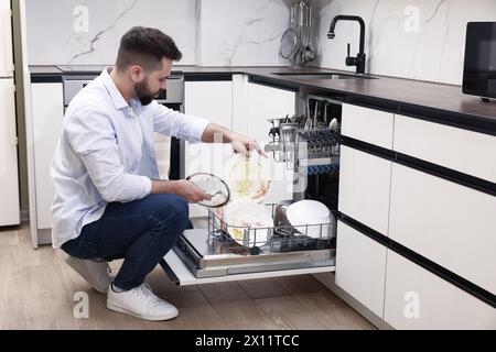 Mann, der in Innenräumen Geschirrspüler mit schmutzigen Tellern lädt Stockfoto