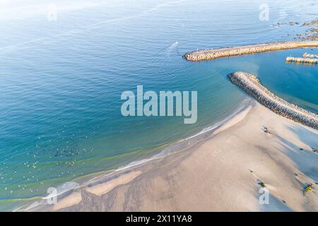 Drohnenansicht eines Fischerbootes, das einen Hafen verlässt, der durch eine Meeresmauer geschützt ist. Ideal für Hintergründe oder Reisekonzepte Stockfoto