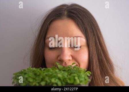 Eine Frau mit geschlossenen Augen und einem ruhigen Ausdruck atmet tief den frischen Duft von lebendigen Mikrogrün ein und deutet auf einen Moment der Verbindung mit der Natur hin. Stockfoto