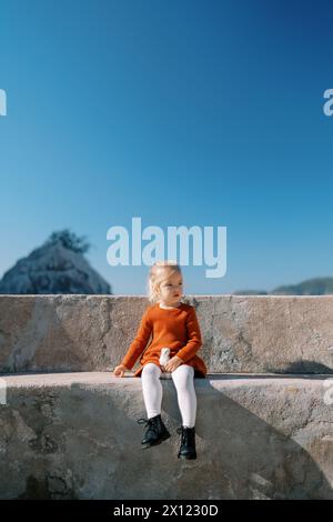 Das kleine Mädchen sitzt auf einer Steinbank auf einer Aussichtsplattform am Meer Stockfoto