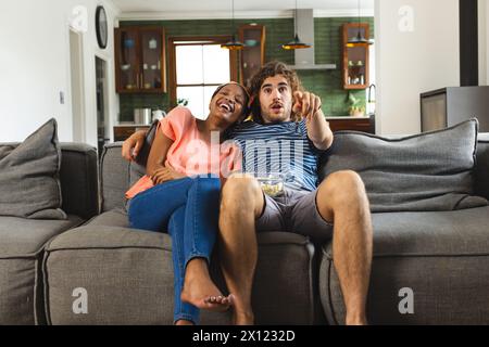 Ein vielseitiges Paar genießt die Zeit auf dem Sofa, zeigt auf etwas, schaut Fernsehen oder Filme zu Hause Stockfoto
